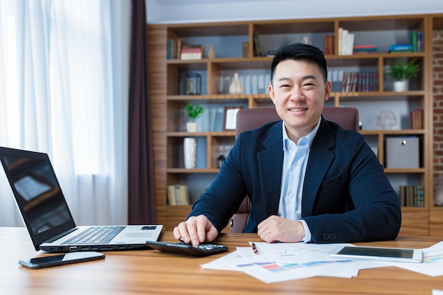 Portrait of young handsome asian man businessman accountant Works with a laptop calculator documents in a suit at the table in the office Smiles