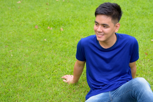 Portrait of young handsome Asian man relaxing at the park in Bangkok, Thailand