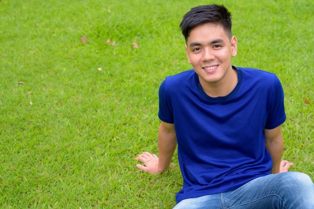 Portrait of young handsome Asian man relaxing at the park in Bangkok, Thailand