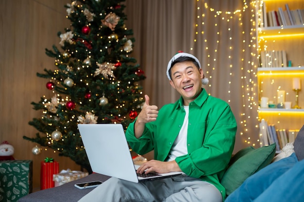 Portrait of a young handsome asian man sitting on the sofa at home near the christmas tree in a red