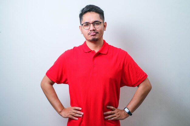 Portrait of young handsome Asian man wearing casual shirt and glasses holding hands on waist Unhappy emotion face expression concept