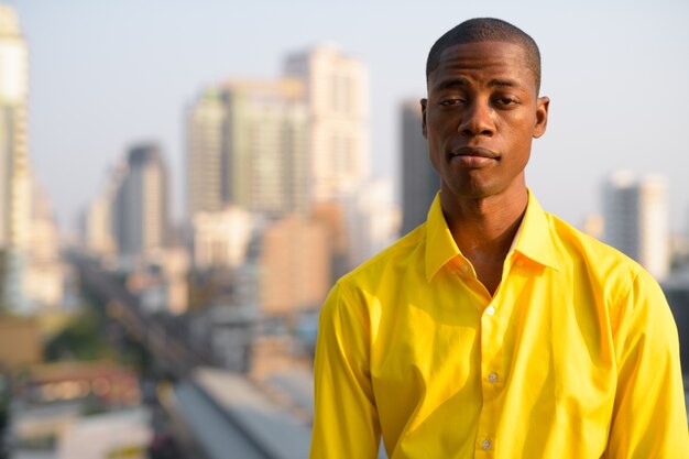 Portrait of young handsome bald African businessman against view of the city