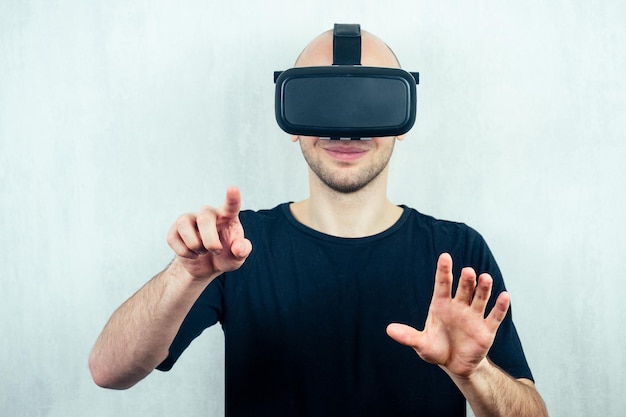 Il ritratto di un giovane uomo calvo bello in una maschera di realtà virtuale (occhiali) punta il dito. il concetto di videogiochi e realtà