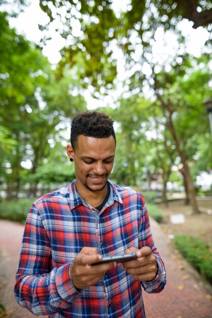 Portrait of young handsome bearded African hipster man at the park outdoors