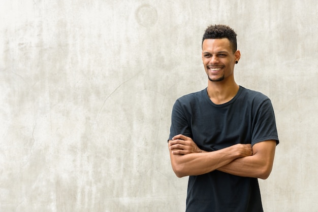 Portrait of young handsome bearded African man against concrete wall outdoors