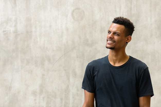 Portrait of young handsome bearded African man against concrete wall outdoors