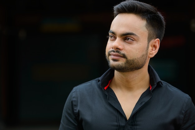 Portrait of young handsome bearded Indian businessman in the city outdoors