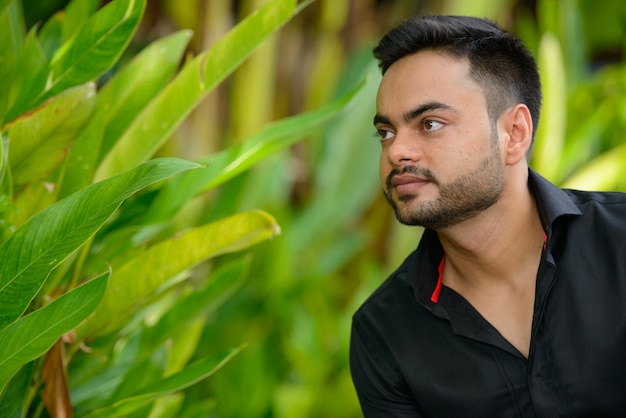 Портрет молодого красивого бородатого индийского бизнесмена в парке на открытом воздухе