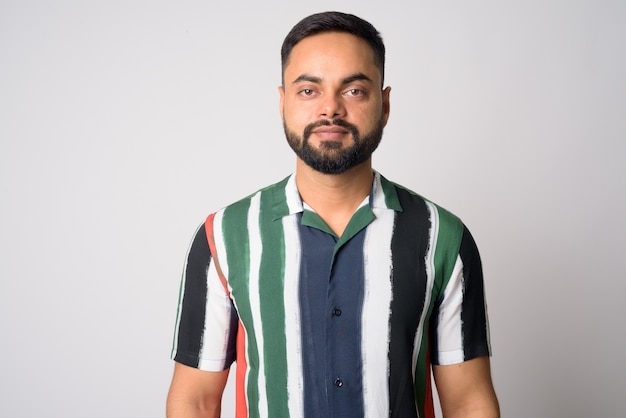 Portrait of young handsome bearded Indian man against white wall