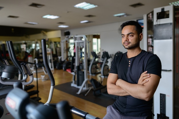 Portrait of young handsome bearded Indian man exercising at the gym