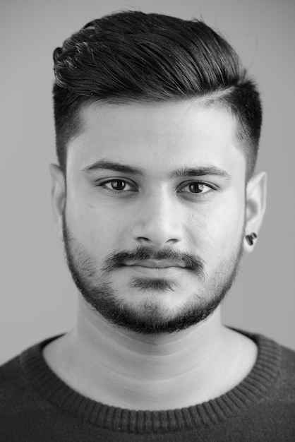 Portrait of young handsome bearded Indian man on white in black and white