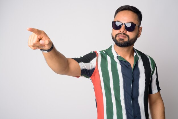 Portrait of young handsome bearded Indian man with sunglasses pointing finger