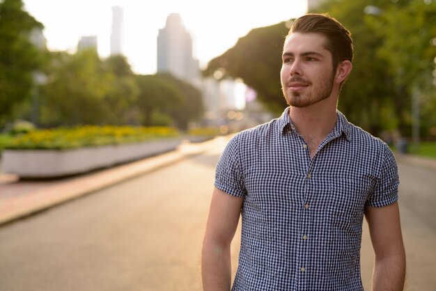 Portrait of young handsome bearded man relaxing at the park outdoors