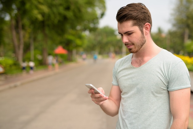 Portrait of young handsome bearded man relaxing at the park outdoors