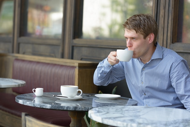 Портрет молодого красивого белокурого бизнесмена, расслабляющегося в кафе на открытом воздухе