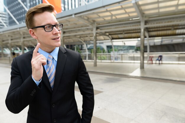 Ritratto di giovane uomo d'affari biondo bello in vestito al ponte dello skywalk nella città all'aperto