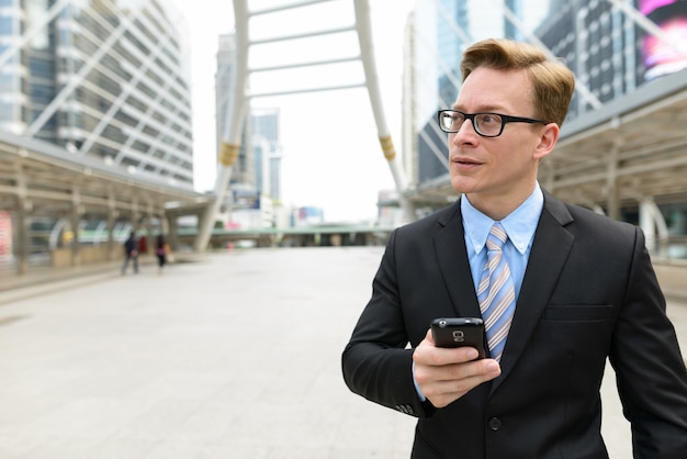 Portrait of young handsome blond businessman in suit at skywalk bridge in the city outdoors