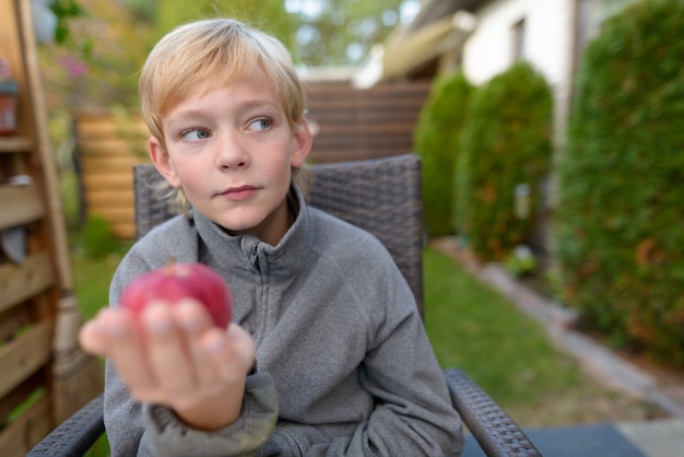 Portrait of young handsome boy with blond hair in the backyard garden at home