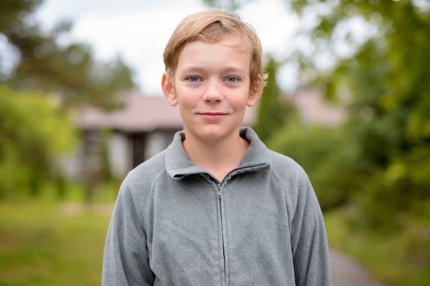 Portrait of young handsome boy with blond hair at home outdoors