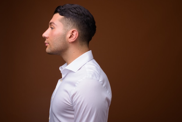 Portrait of young handsome businessman against brown wall