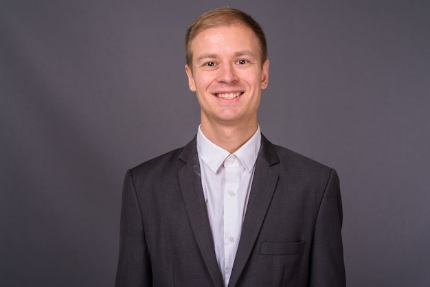 Portrait of young handsome businessman against gray wall