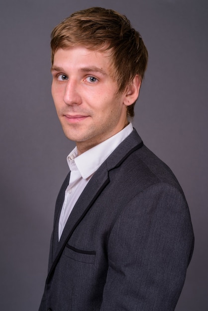 Portrait of young handsome businessman against gray wall