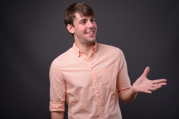 Portrait of young handsome businessman against gray wall