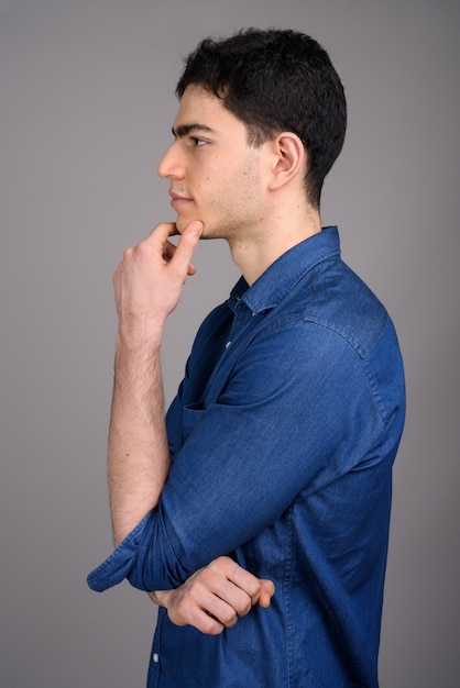 Portrait of young handsome businessman against gray