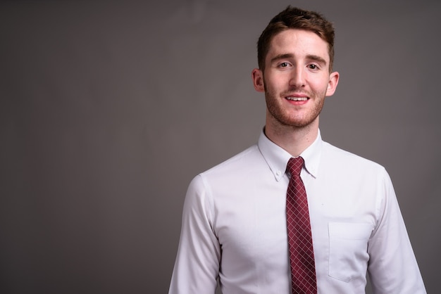 Portrait of young handsome businessman against gray