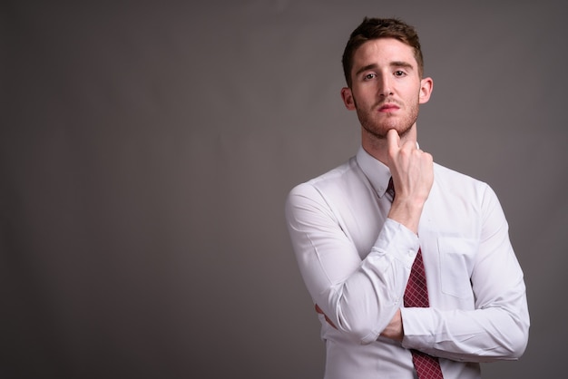 Portrait of young handsome businessman against gray