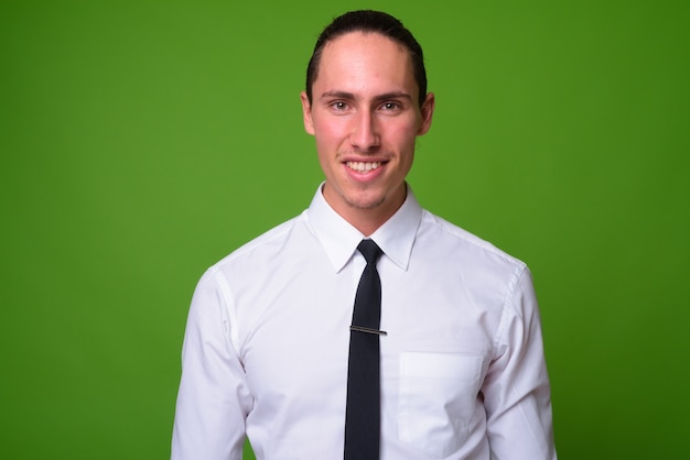 Portrait of young handsome businessman against green wall