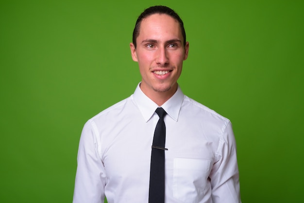 Portrait of young handsome businessman against green wall