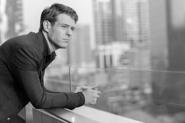 Portrait of young handsome businessman in suit against view of the city in black and white