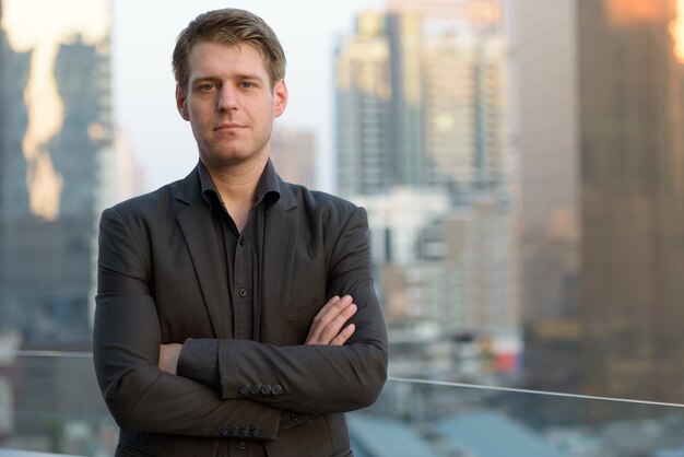 Portrait of young handsome businessman in suit against view of the city