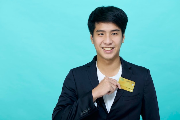 Portrait Young handsome businessman in a suit holding yellow credit card isolated in a blue studio