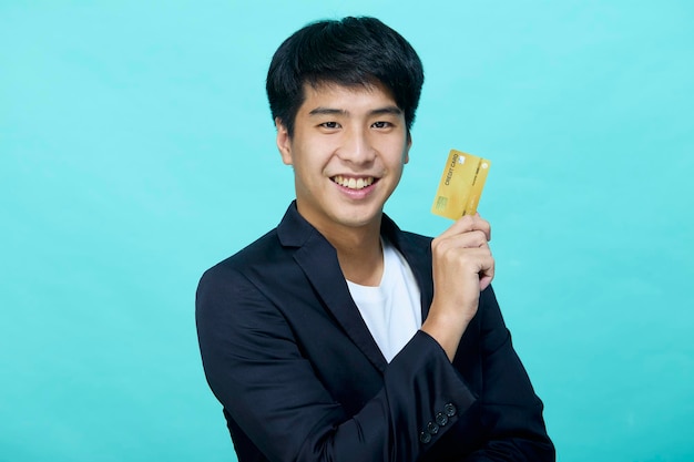 Portrait Young handsome businessman in a suit holding yellow credit card isolated in a blue studio