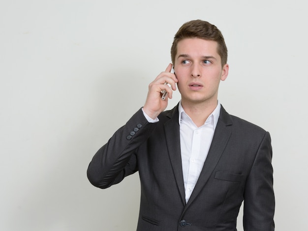 Portrait of young handsome businessman wearing suit against white wall