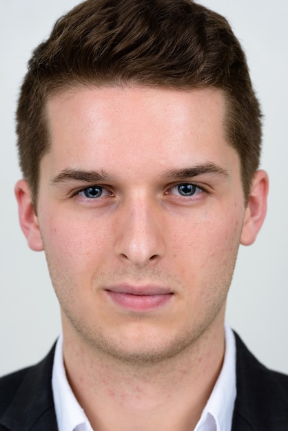 Portrait of young handsome businessman wearing suit against white wall