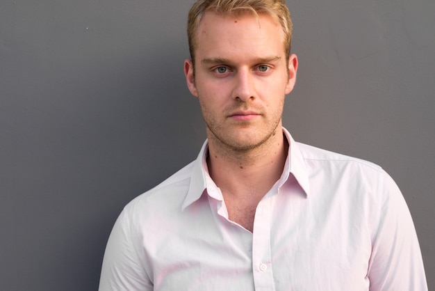 Portrait of young handsome businessman with blond hair against gray wall