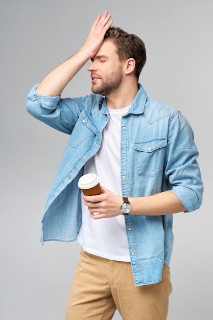 Ritratto di giovane uomo caucasico bello in camicia di jeans che tiene tazza di caffè per andare