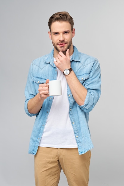 Portrait of young handsome caucasian man in jeans shirt holding cup of coffee