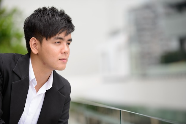 Portrait of young handsome Filipino businessman against view of the city outdoors