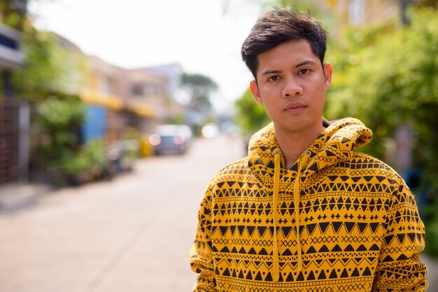 Portrait of young handsome Filipino man wearing hoodie in the streets outdoors