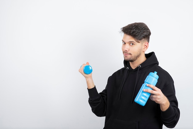 Portrait of young handsome guy holding blue dumbbell and water bottle