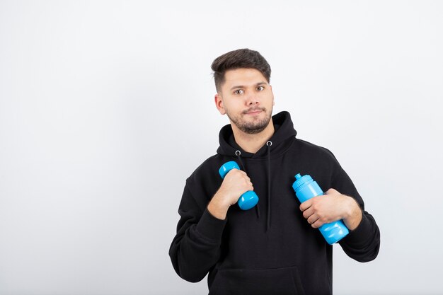 Portrait of young handsome guy holding blue dumbbell and water bottle