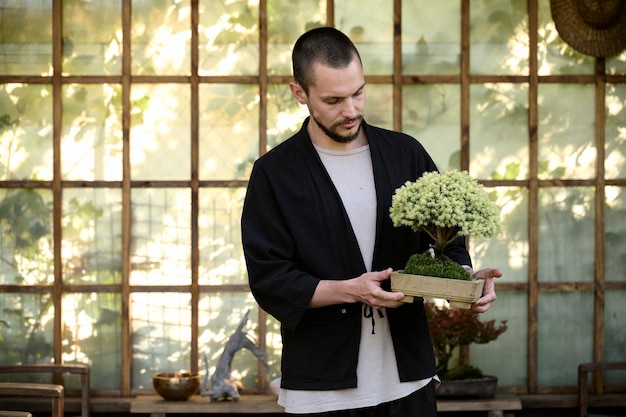 Portrait of a young handsome guy with a bonsai in his hands on the background of an Asian tea house