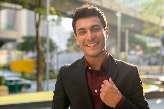 Portrait of young handsome Hispanic businessman in the city streets outdoors