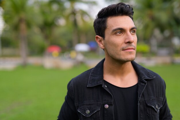 Portrait of young handsome Hispanic man in the park outdoors