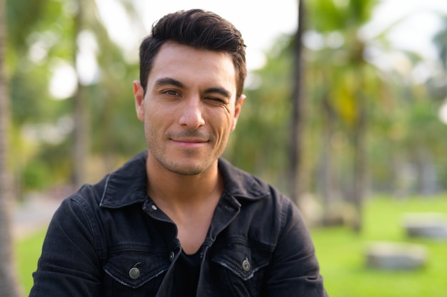 Portrait of young handsome Hispanic man in the park outdoors