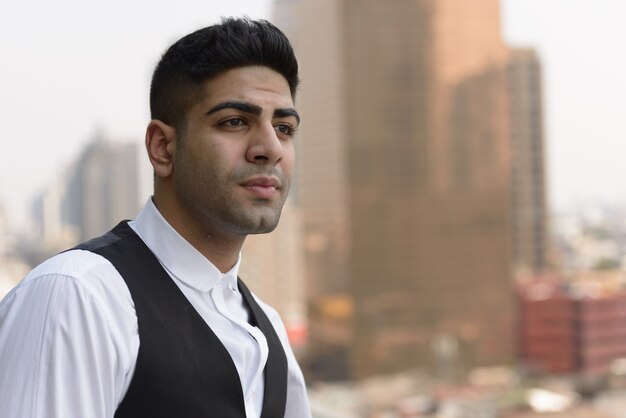 Portrait of young handsome Indian businessman against view of the city